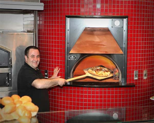 chef smiling at the camera as he places a pizza into the oven
