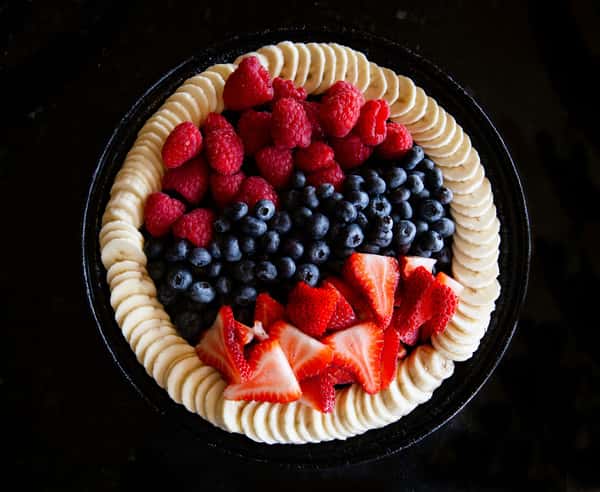 fruit tart topped with strawberries, blueberries, and banana slices in a decorative pattern