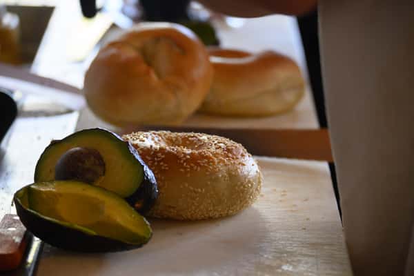 Sliced avocado beside a sesame bagel on a prep station in a bagel shop kitchen