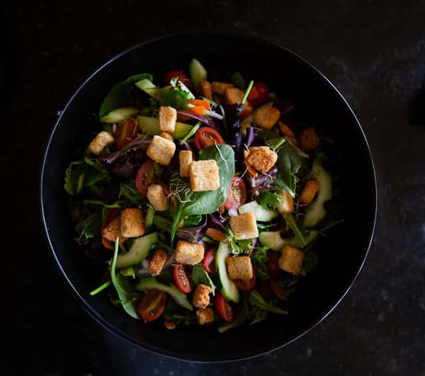 mixed greens salad with croutons, vegetables, and cheese in a dark bowl