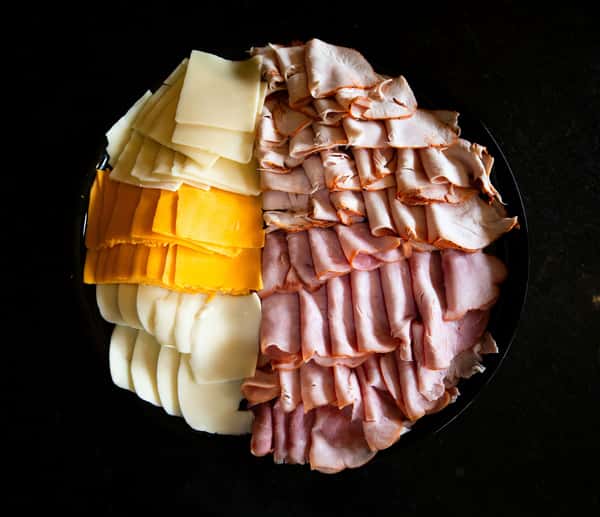 assorted sliced deli meats and cheeses arranged in a circular charcuterie display