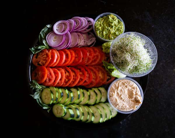 fresh vegetable platter with sliced cucumbers, tomatoes, red onions, and dips arranged on a board