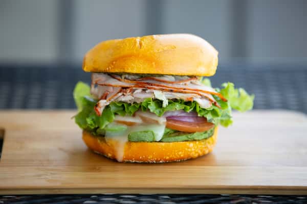 stacked deli sandwich with assorted meats, cheese, lettuce, and tomato on a soft bun