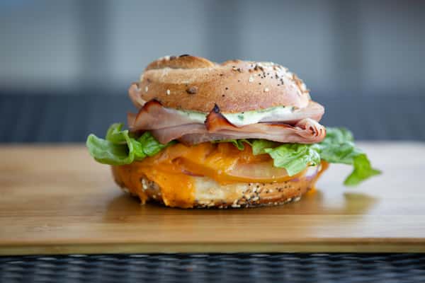 bagel sandwich with sliced deli meat, melted cheese, and greens on a toasted everything bagel