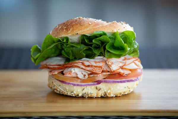 bagel sandwich with sliced turkey, lettuce, tomato, and red onion on a toasted bun