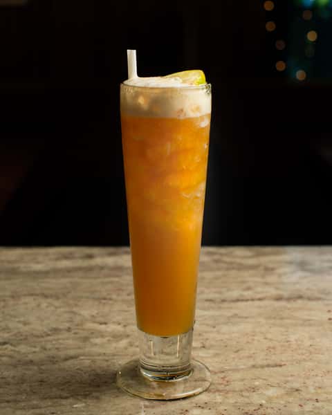 Iced citrus cocktail with frothy top and lemon garnish, served in a tall glass on a marble bar in an upscale lounge