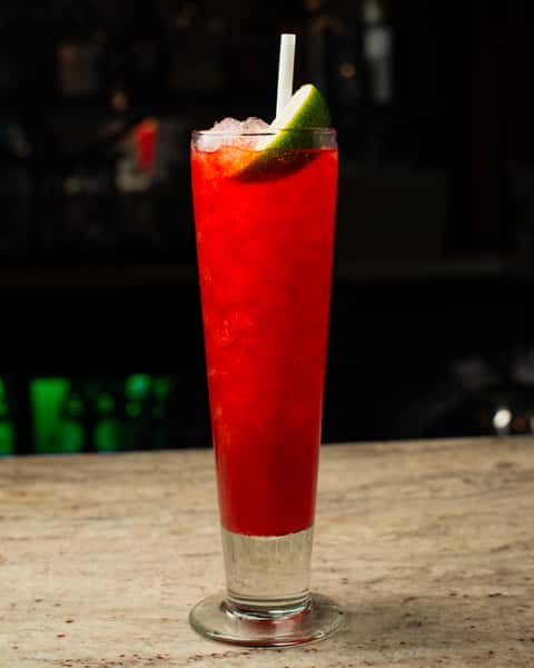 Refreshing red iced cocktail with lime wedge and straw, served in a tall glass on a marble bar in a modern lounge setting