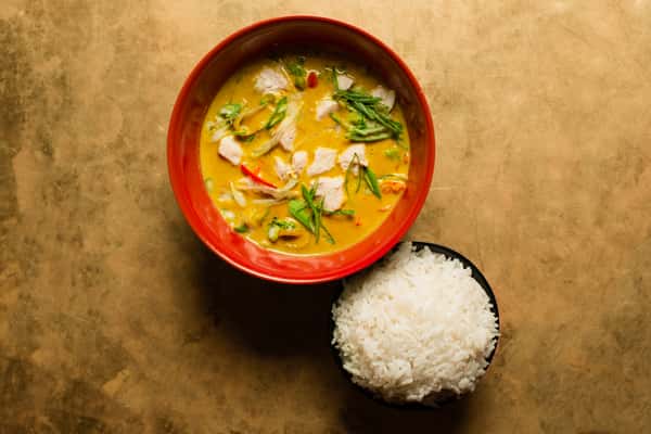 Creamy Thai-style chicken coconut curry with fresh herbs, served in a red bowl alongside steamed white rice in a modern Asian restaurant