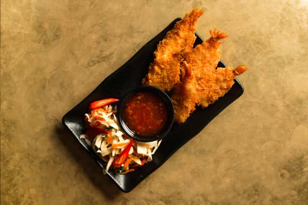 Crispy golden shrimp tempura served on a sleek black plate with tangy dipping sauce and fresh Asian slaw, styled in a modern Japanese restaurant setting