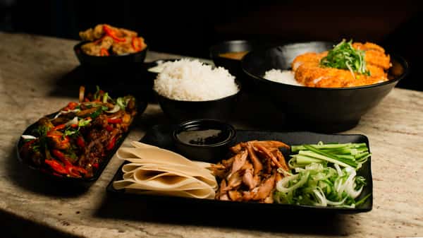 Assorted Asian dishes including crispy tonkatsu, stir-fried beef, and rice bowls, presented on a marble table in a stylish restaurant setting