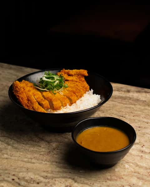 Japanese tonkatsu breaded pork cutlet over steamed rice with curry sauce on the side, served in a modern black bowl