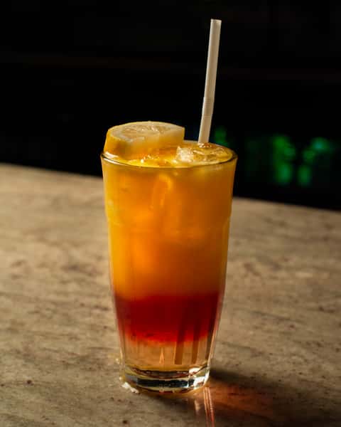 Refreshing layered iced citrus drink with lemon slice and straw, featuring a vibrant orange-to-red gradient, served on a marble table in a stylish restaurant setting