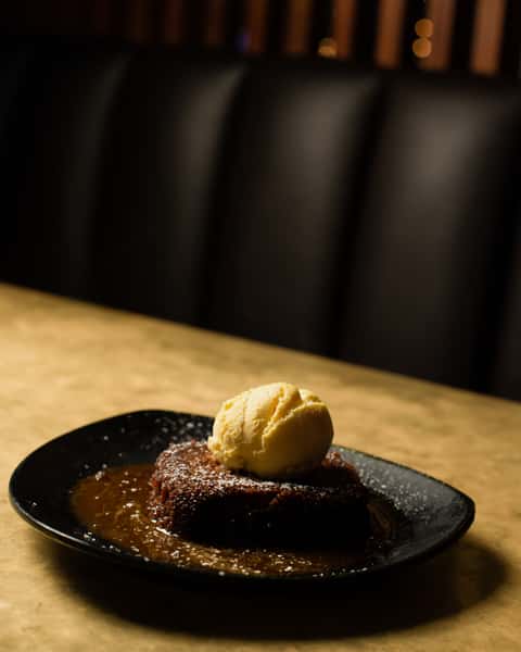 Warm chocolate dessert topped with vanilla ice cream, served on a black plate in a cozy restaurant setting