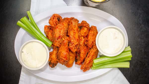 Buffalo chicken wings with celery sticks and two bowls of ranch dressing on a white platter.