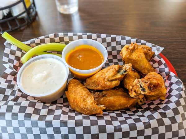 Buffalo wings with celery sticks and ranch dressing, plus a side of onion rings, served on checkered paper.