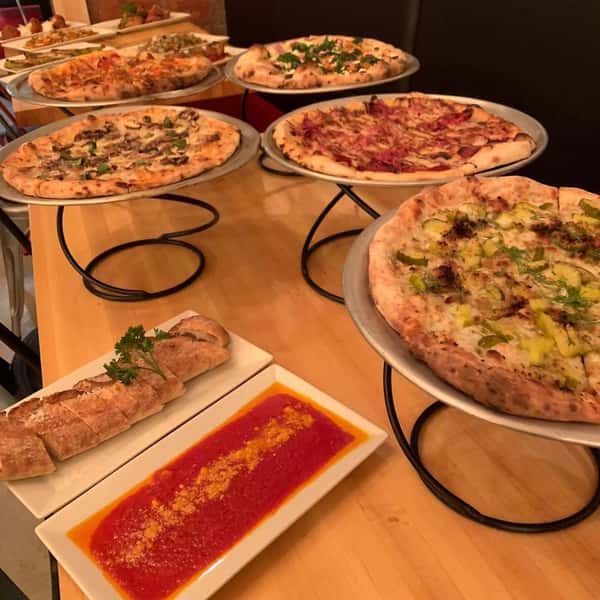 Variety of pizzas on a wooden table with sauce on side