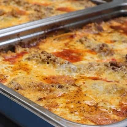 Close-up of freshly baked cheesy meat lasagna in a stainless steel tray, featuring golden brown crust and rich tomato sauce.