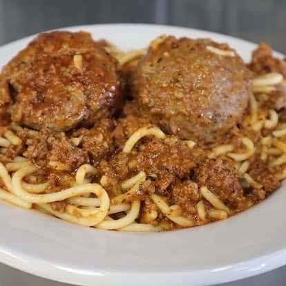 Hearty plate of spaghetti with meat sauce and two large Italian-style meatballs, served on a white ceramic dish.