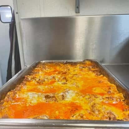 Large pan of cheesy baked lasagna with bubbling layers of meat sauce and melted mozzarella, fresh from the oven in a commercial kitchen.