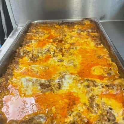 Full tray of hot, bubbling beef lasagna with rich tomato sauce and melted cheese, fresh from a commercial oven.