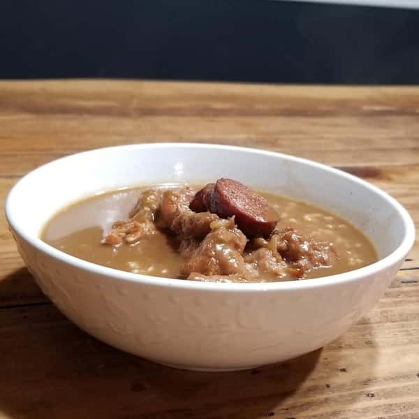 Bowl of creamy red beans with sausage slices and slow-cooked meat, served in a rustic setting on a wooden table.
