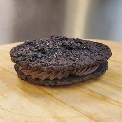 Rich double chocolate cookie sandwich with creamy chocolate frosting and a sprinkle of crushed Oreos on a wooden surface.