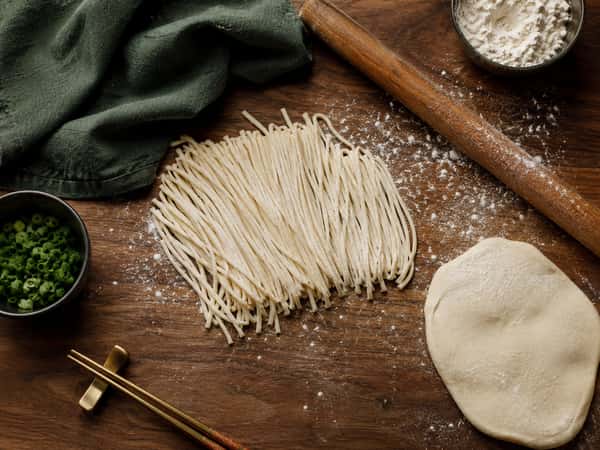 Fresh handmade Asian noodles and rolled dough on a floured wooden surface at Tora Asian House