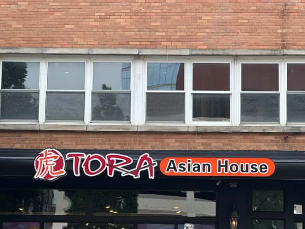 Tora Asian House restaurant storefront featuring the illuminated TORA Asian House sign on a brick building