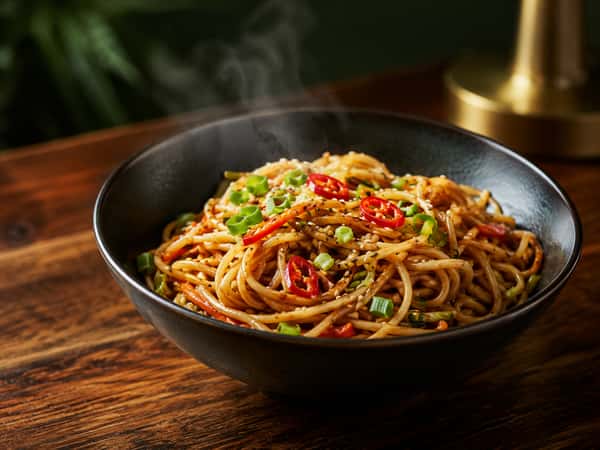 Steaming Asian stir-fried noodles topped with green onions, red chili peppers, and sesame seeds at Tora Asian House