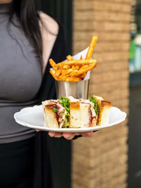 Thick-cut turkey sandwich with greens and cranberry sauce on white bread, served with golden French fries in a metal cup.