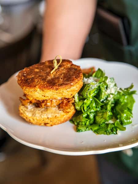 Fried chicken biscuit sandwich served with a side of fresh arugula salad topped with shredded cheese.