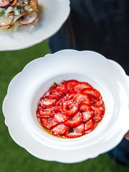 Thinly sliced strawberries arranged in a rosette pattern over a syrupy glaze, served on an elegant white plate.