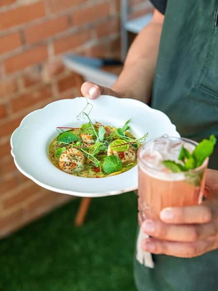 Seared scallops in a light broth garnished with fresh herbs and microgreens, served with a refreshing mint cocktail.
