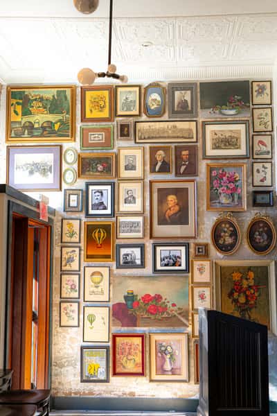 Eclectic gallery wall featuring vintage portraits, floral still lifes, hot air balloons, and historic scenes in ornate and colorful frames.