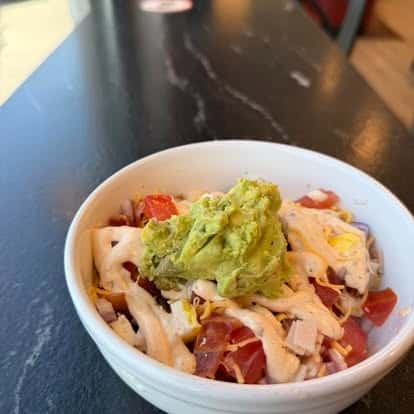 Burrito bowl with rice, chicken, and toppings, topped with a scoop of guacamole