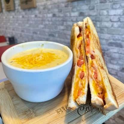 Bowl of orange soup with a grilled sandwich cut into triangles on a wooden board