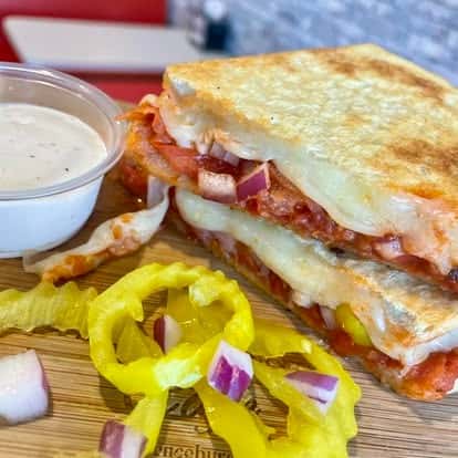 Grilled sandwich cut into triangles, served with pepperoncini, red onion, and dipping sauce