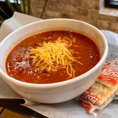 Bowl of chili topped with shredded cheese, served with saltine crackers