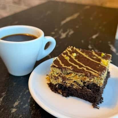 Slice of chocolate brownie with caramel drizzle, served with a cup of coffee