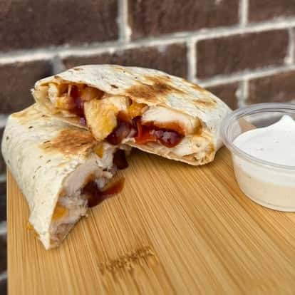 Chicken and berry quesadilla wrap, cut in half, served with a side of sour cream on a wooden board