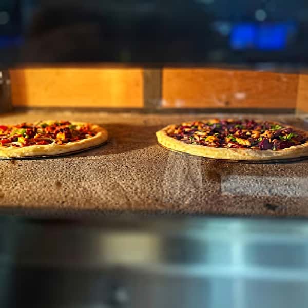 Fresh vegetable pizzas baking directly on a hot stone in a restaurant pizza oven