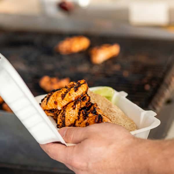 Freshly grilled seasoned chicken served in a takeout container with flatbread and lime