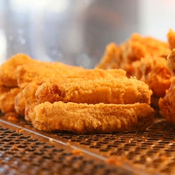 Freshly fried golden battered fish fillets resting on a fryer rack at a fish and chips restaurant