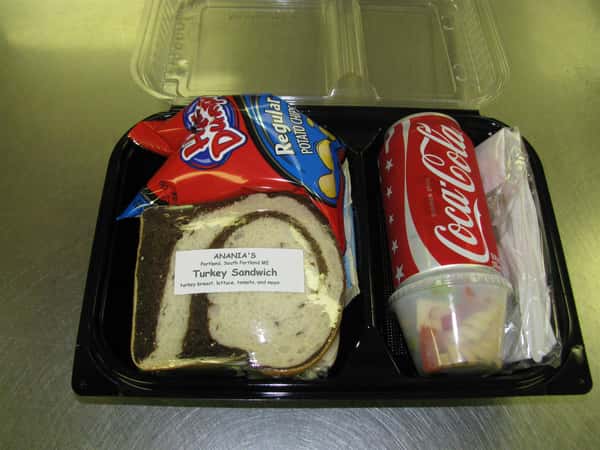Lunch container with a turkey sandwich, bag of chips, a can of Coca Cola and a small cup of pasta salad