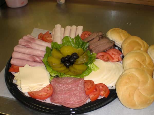 Deli platter with deli meats, cheese, tomatoes and pickles and rolls on the side