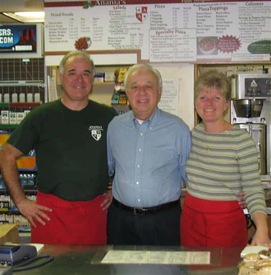Three staff members smiling with their arms around each other behind the counter