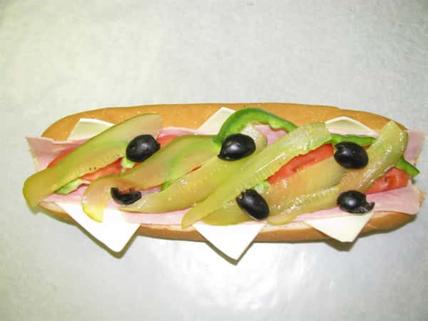 Sub with cheese, deli meats, green peppers. olives and pickles on top