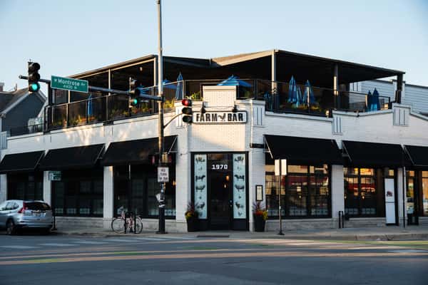 Exterior of Farmbar in Ravenswood, Chicago. It's a white brick building with blue umbrellas on top and a covering from the sun