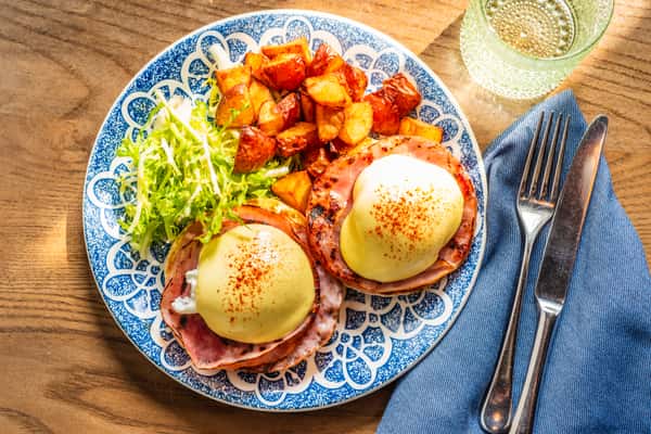 eggs benedict sits on a blue plate by a fork and glass of water