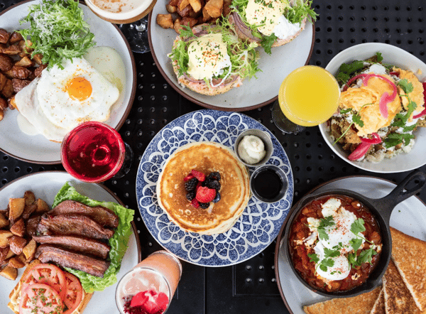 a black table with blue plates that have breakfast foods on them: stack of pancakes with berries, over easy eggs, breakfast potatoes and sausages